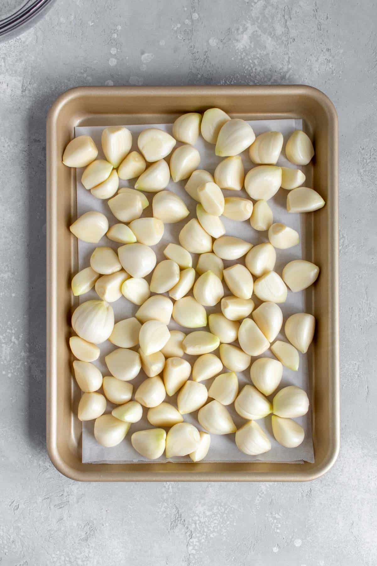 Garlic cloves on a lined sheet pan.