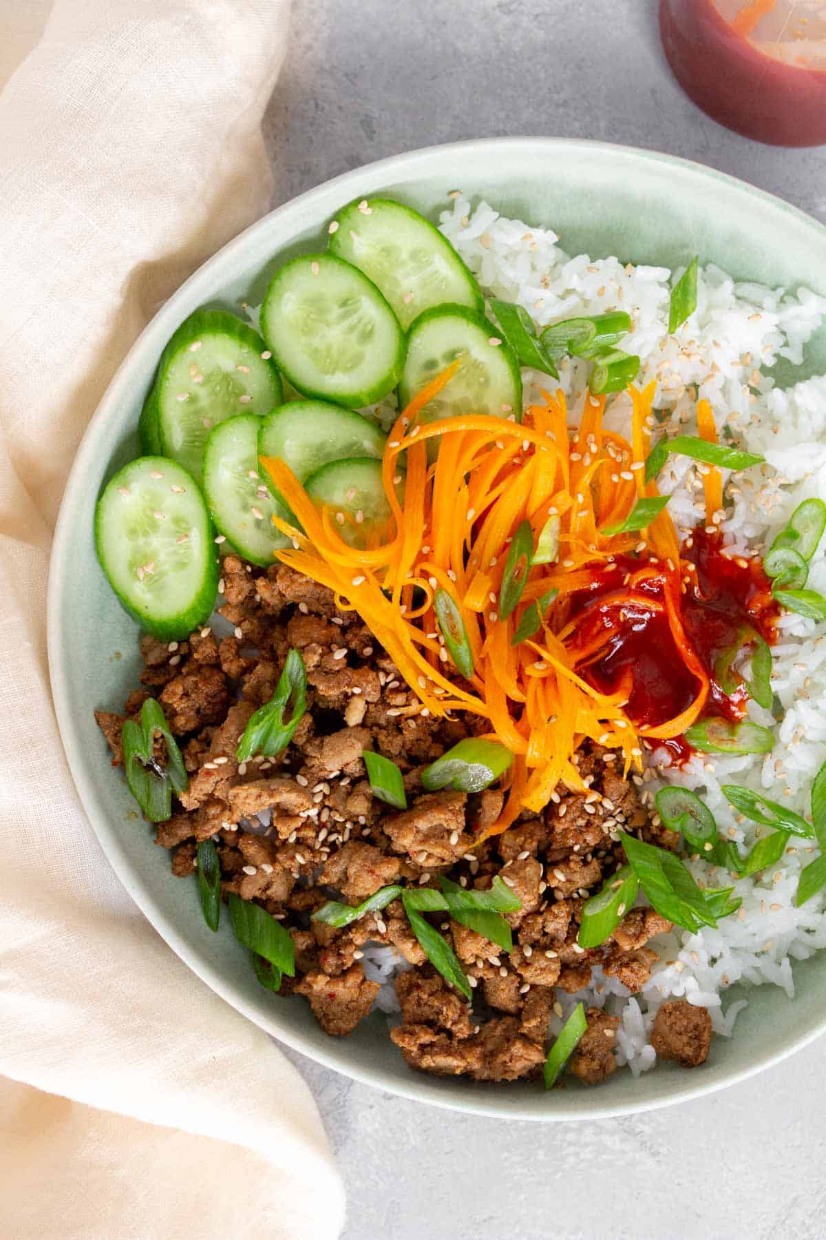 Overhead view of a closer view of ground turkey, cucumber, carrots, sauce, green onions, and rice.