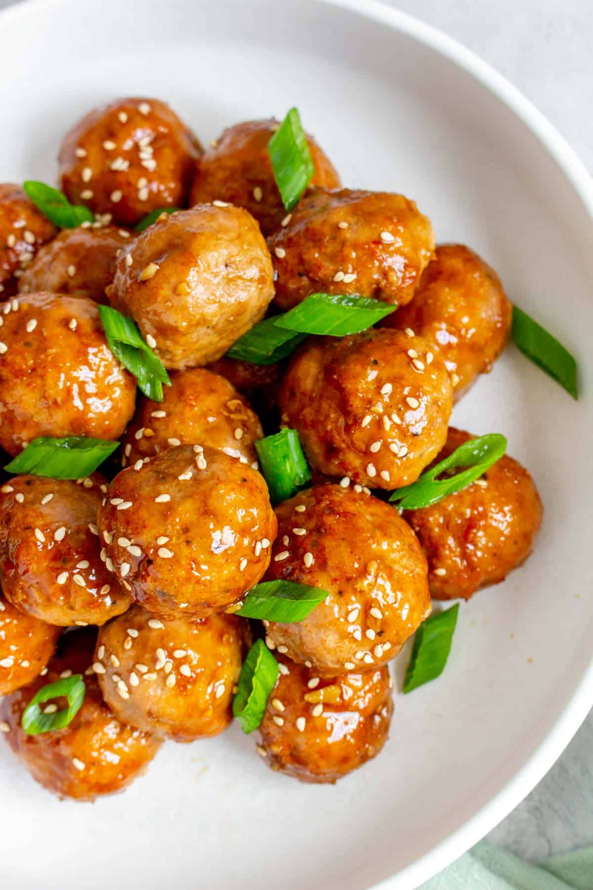 Overhead view of a pile of teriyaki turkey meatballs on a plate with green onions and sesame seeds.