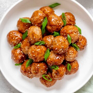 Close view of an overhead view of a plate of teriyaki turkey meatballs with sesame seeds and green onions on top.
