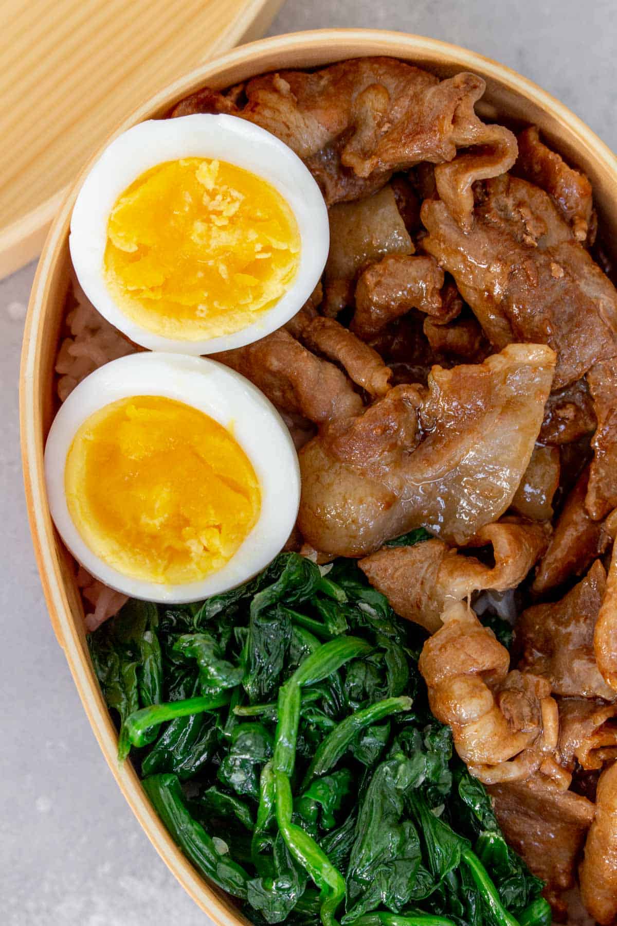 Close up of eggs in a bento with pork and spinach.