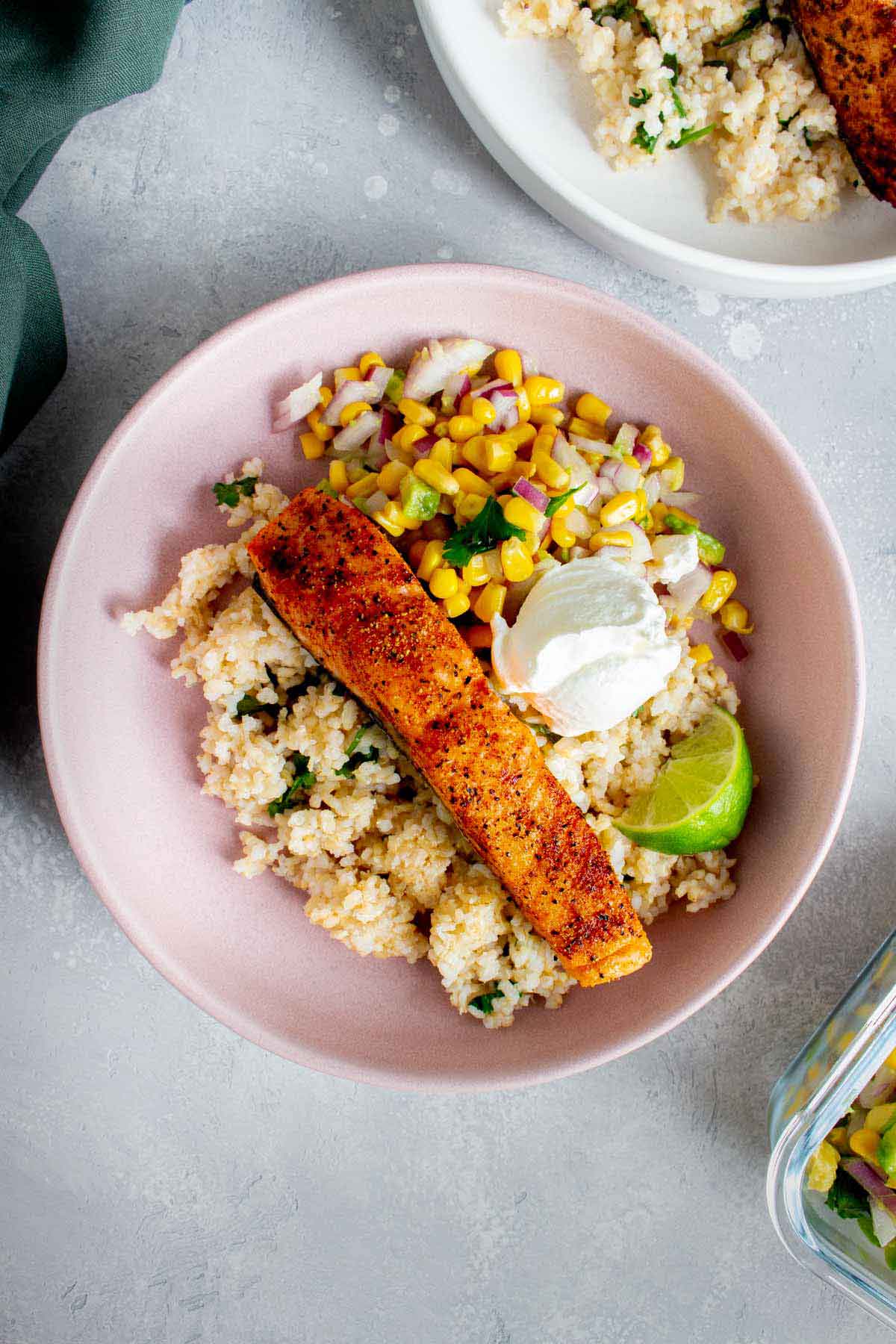 Overhead view of a plate of air fryer salmon on top of brown rice, corn salsa, and sour cream.