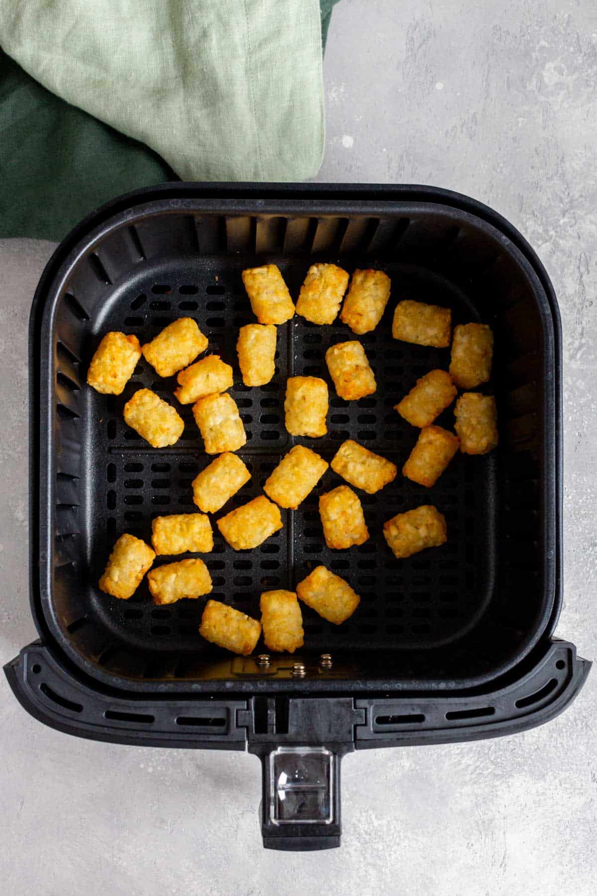 Overhead view of air fried tater tots in an air fryer basket.