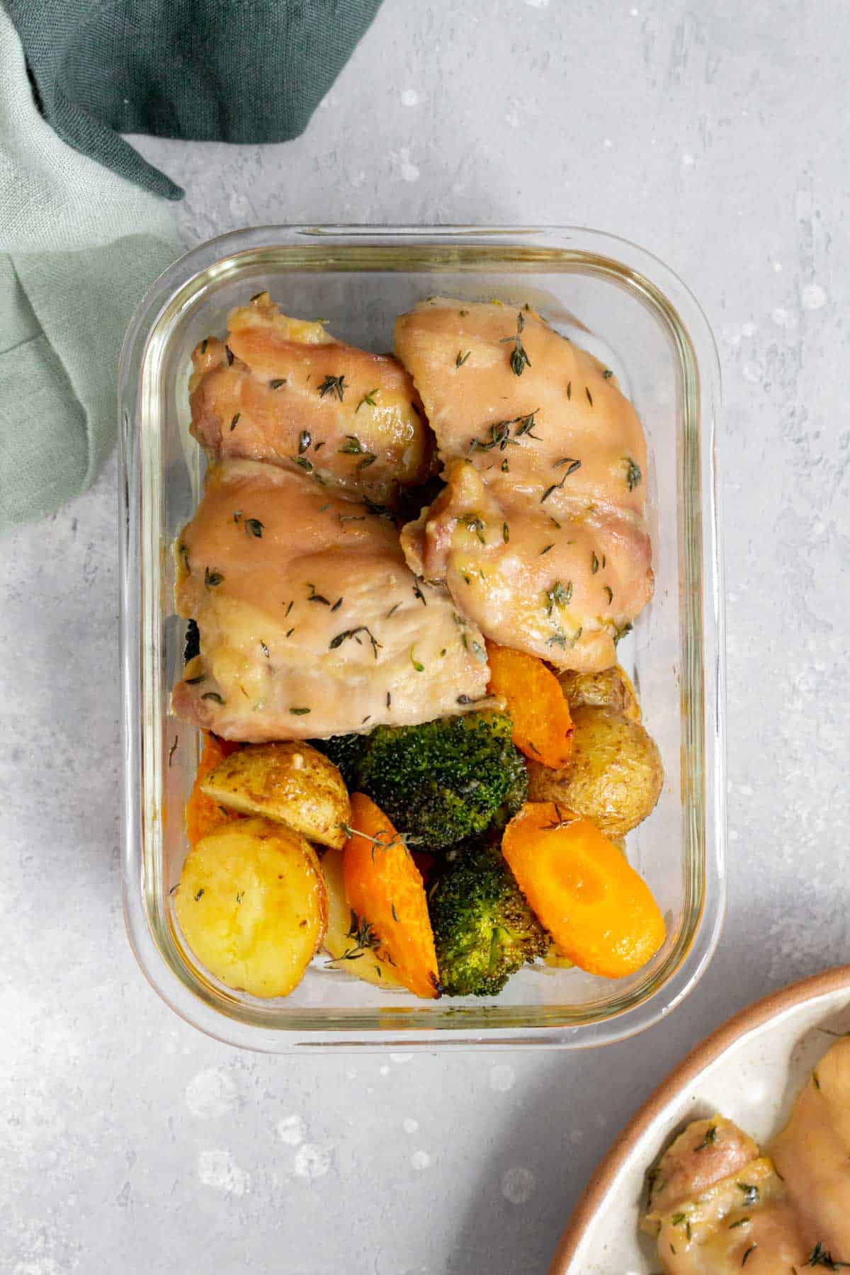 A meal prep container with chicken thighs with a side of broccoli, carrots, and potatoes.