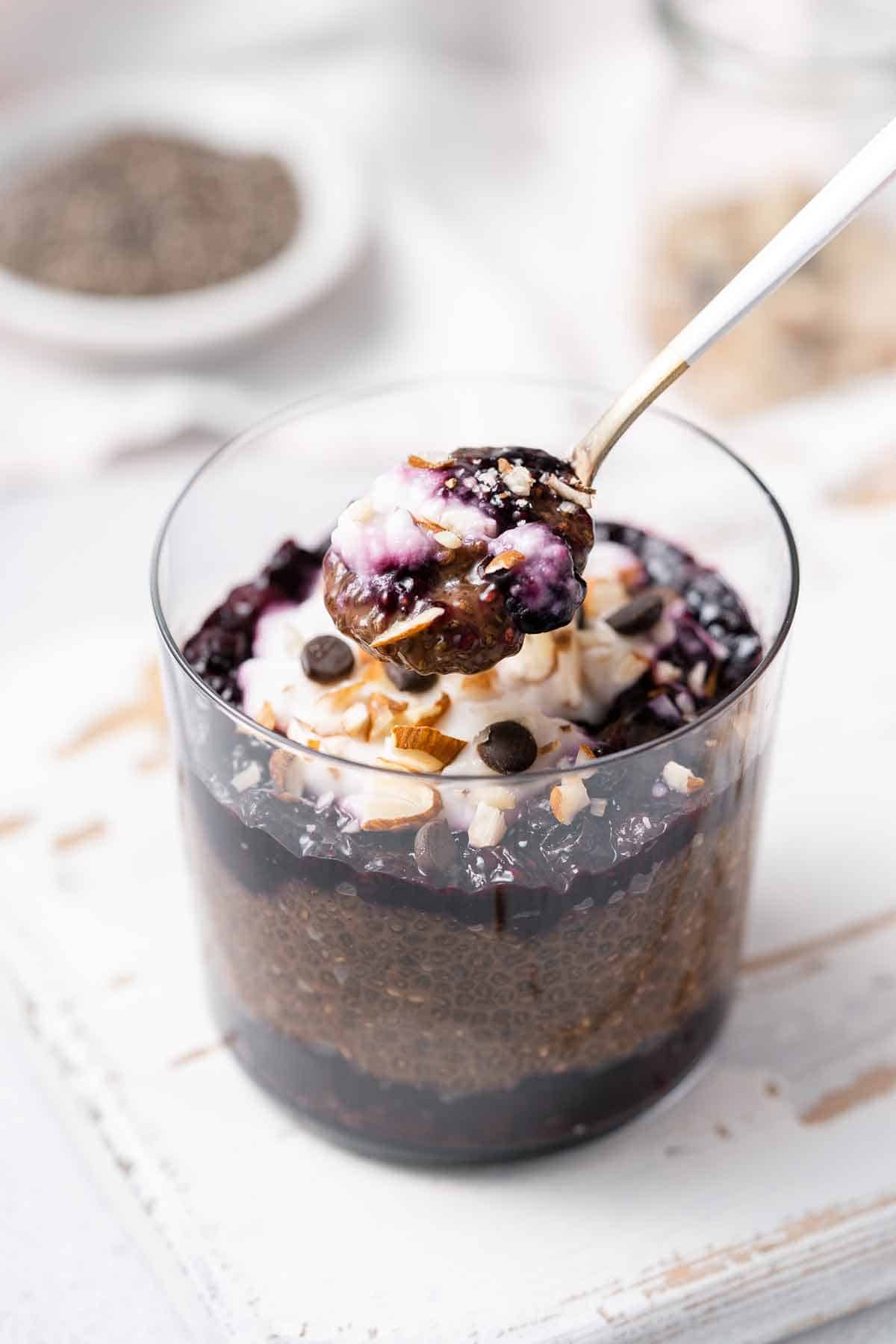 A glass of chocolate blueberry chia pudding with a spoonful lifted up.