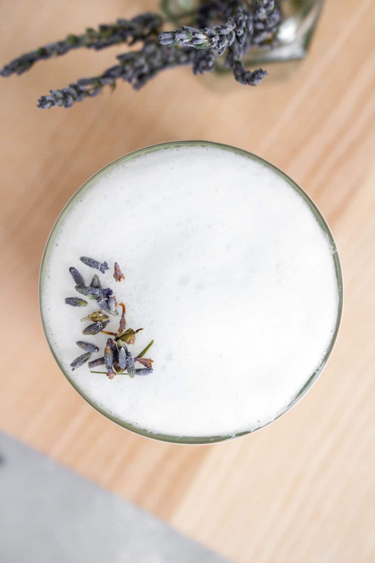 Overhead view of a glass of lavender london fog with lavender buds on top.