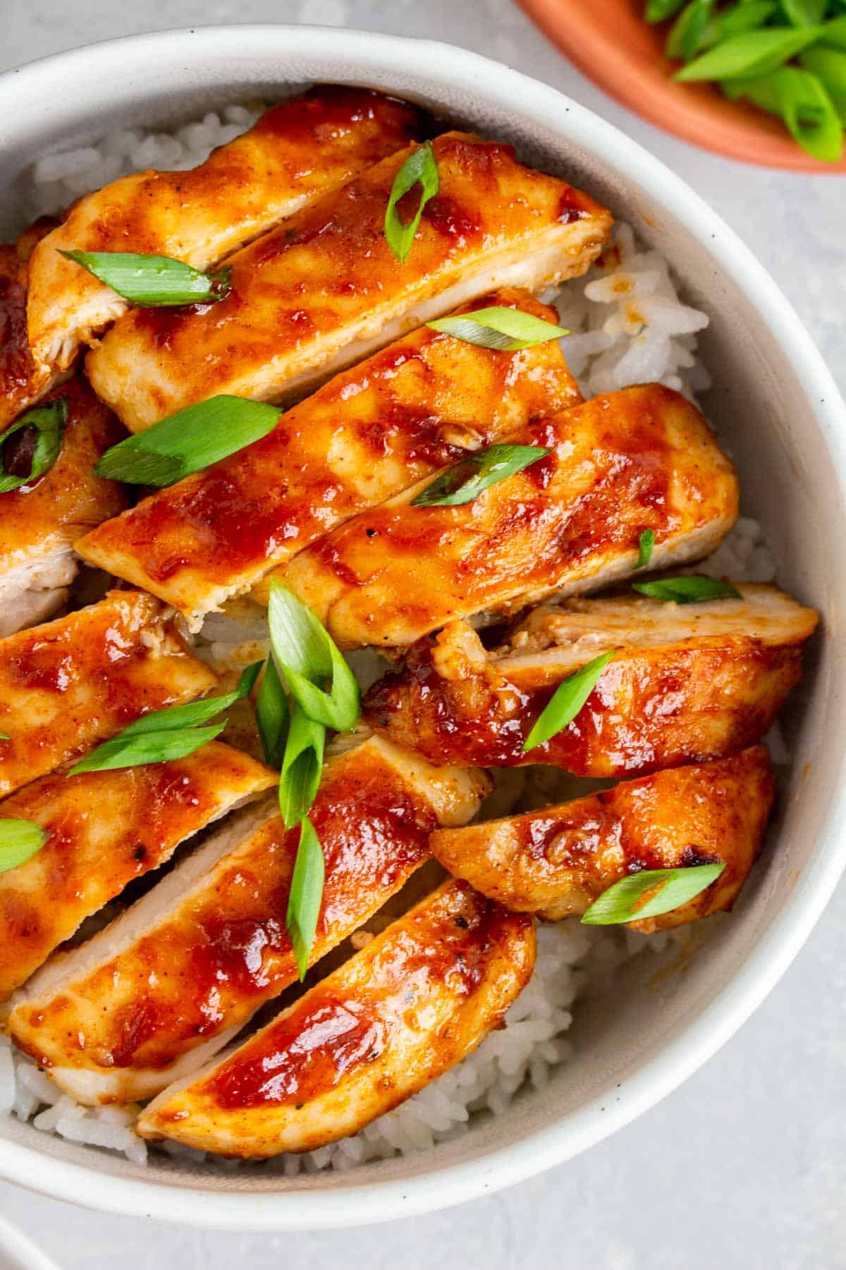 Close up of sliced air fryer bbq chicken over rice, garnished with green onions.