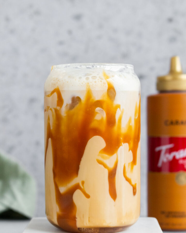 A glass of iced caramel latte with caramel drizzled inside the glass.