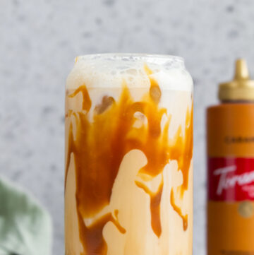 A glass of iced caramel latte with a bottle of caramel in the background.