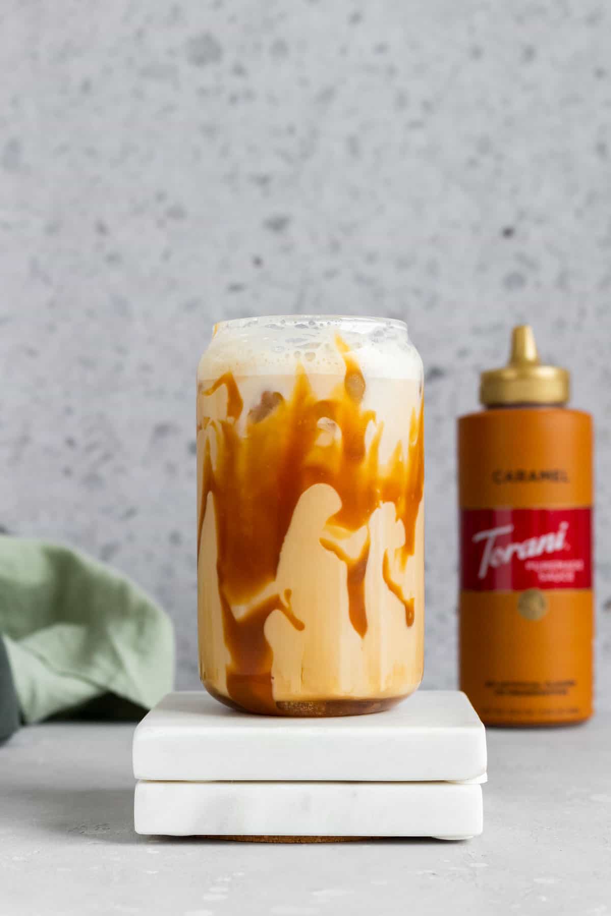 A glass of iced caramel latte with caramel drizzled inside the glass on top of two coasters.
