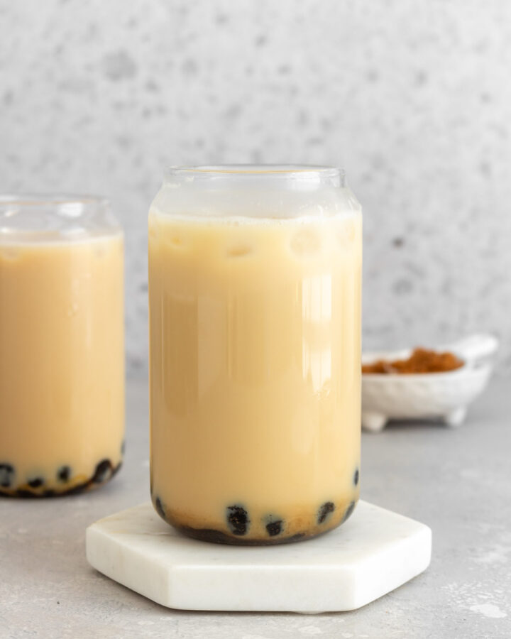 A glass of jasmine milk tea on a coaster in front of a second glass in the background.