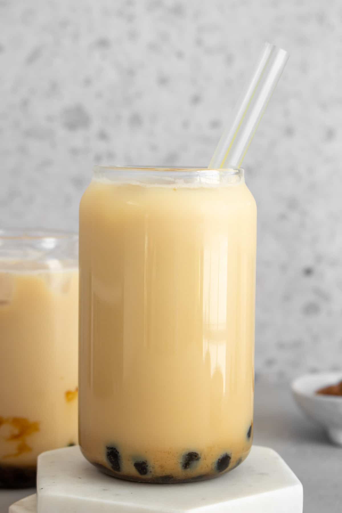 A glass of jasmine milk tea with tapioca with a straw.
