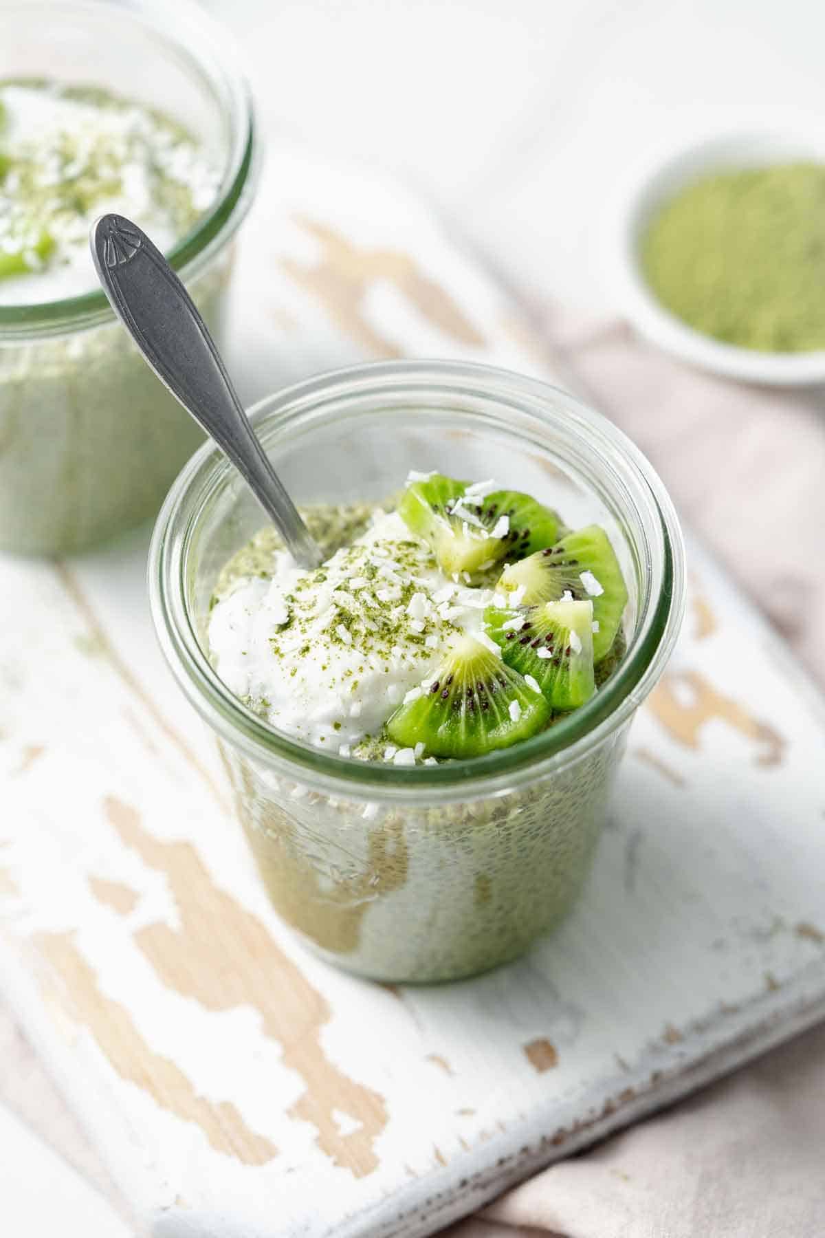 Angled view of a cup of matcha chia pudding with yogurt and kiwi on top.