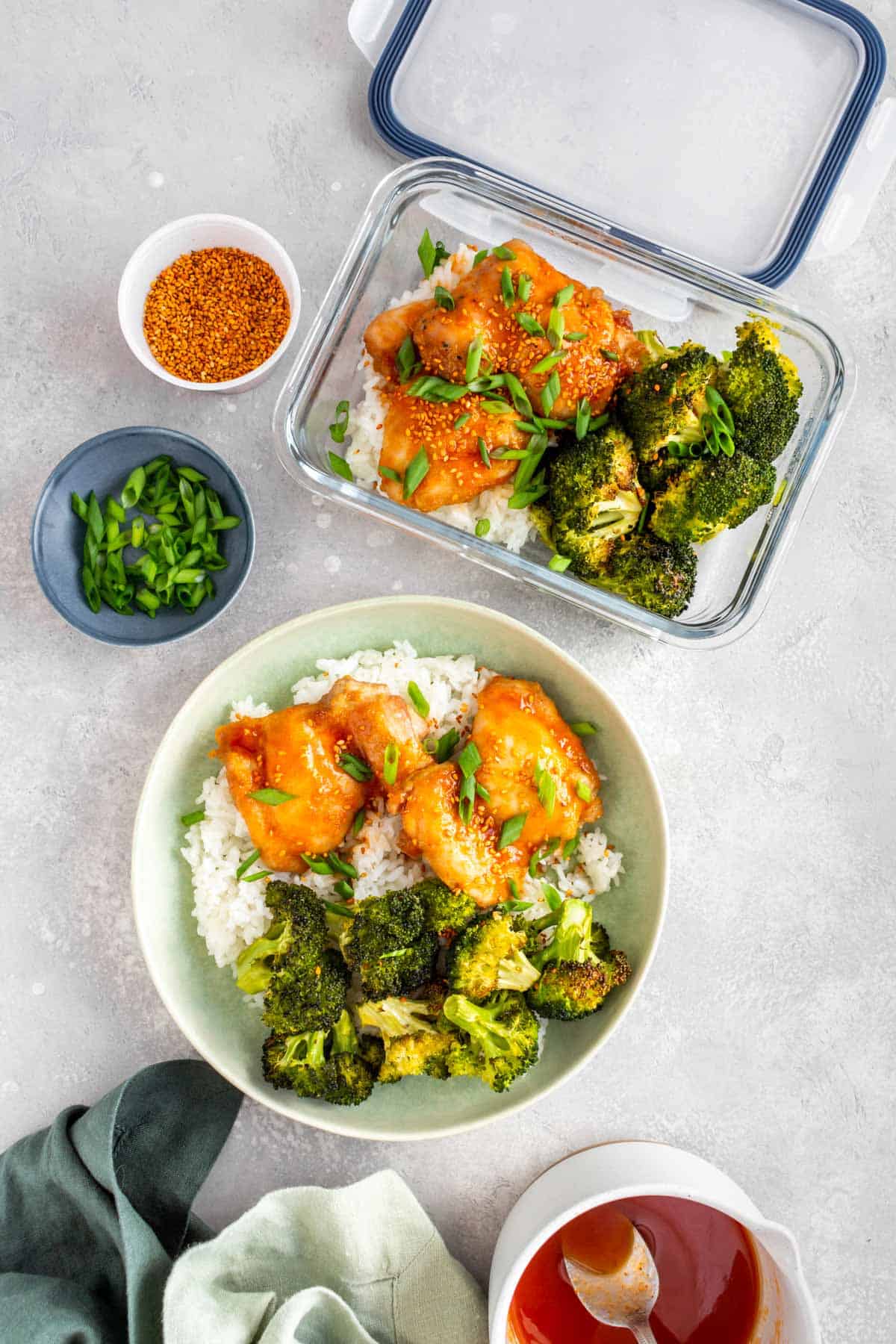 Overhead view of a bowl and meal prep container of sheet pan chicken thighs and broccoli with honey sriracha glaze with rice.
