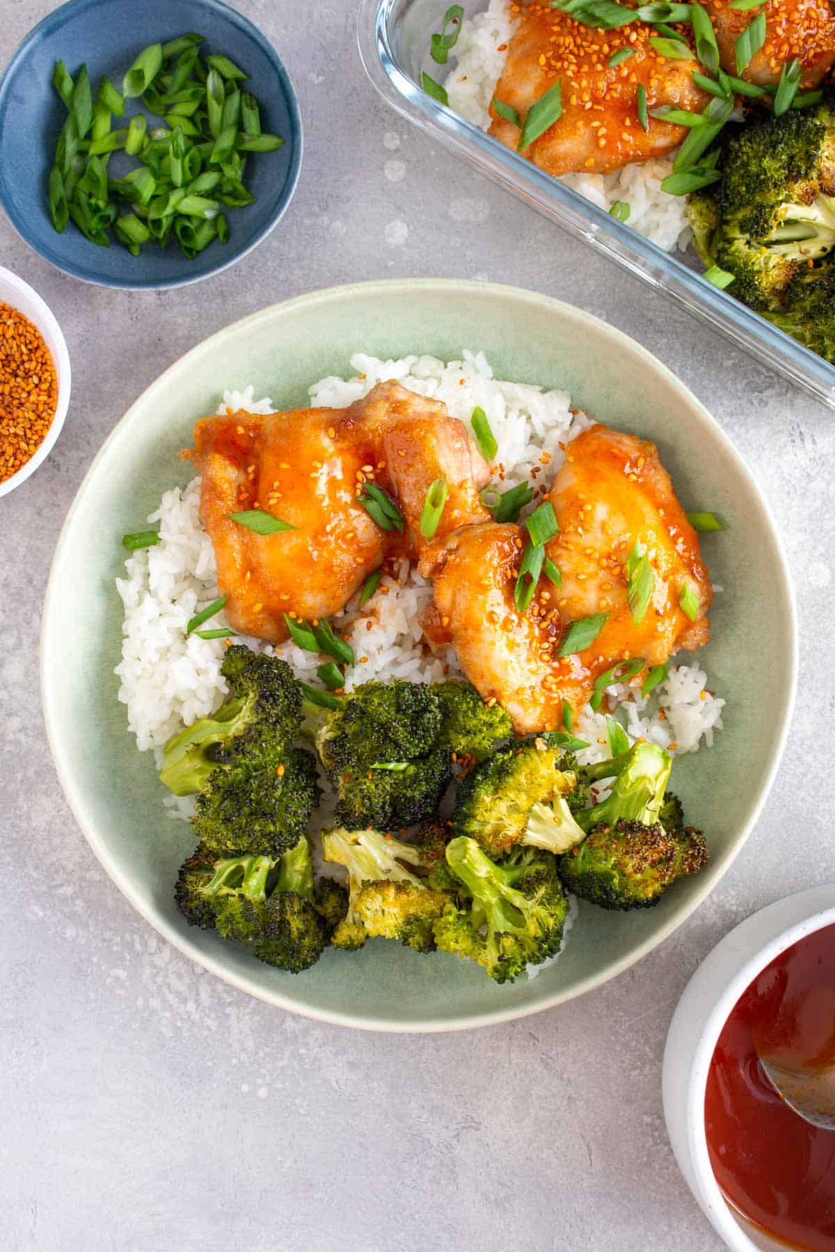A plate of rice underneath sheet pan chicken thighs and broccoli with honey sriracha glaze.
