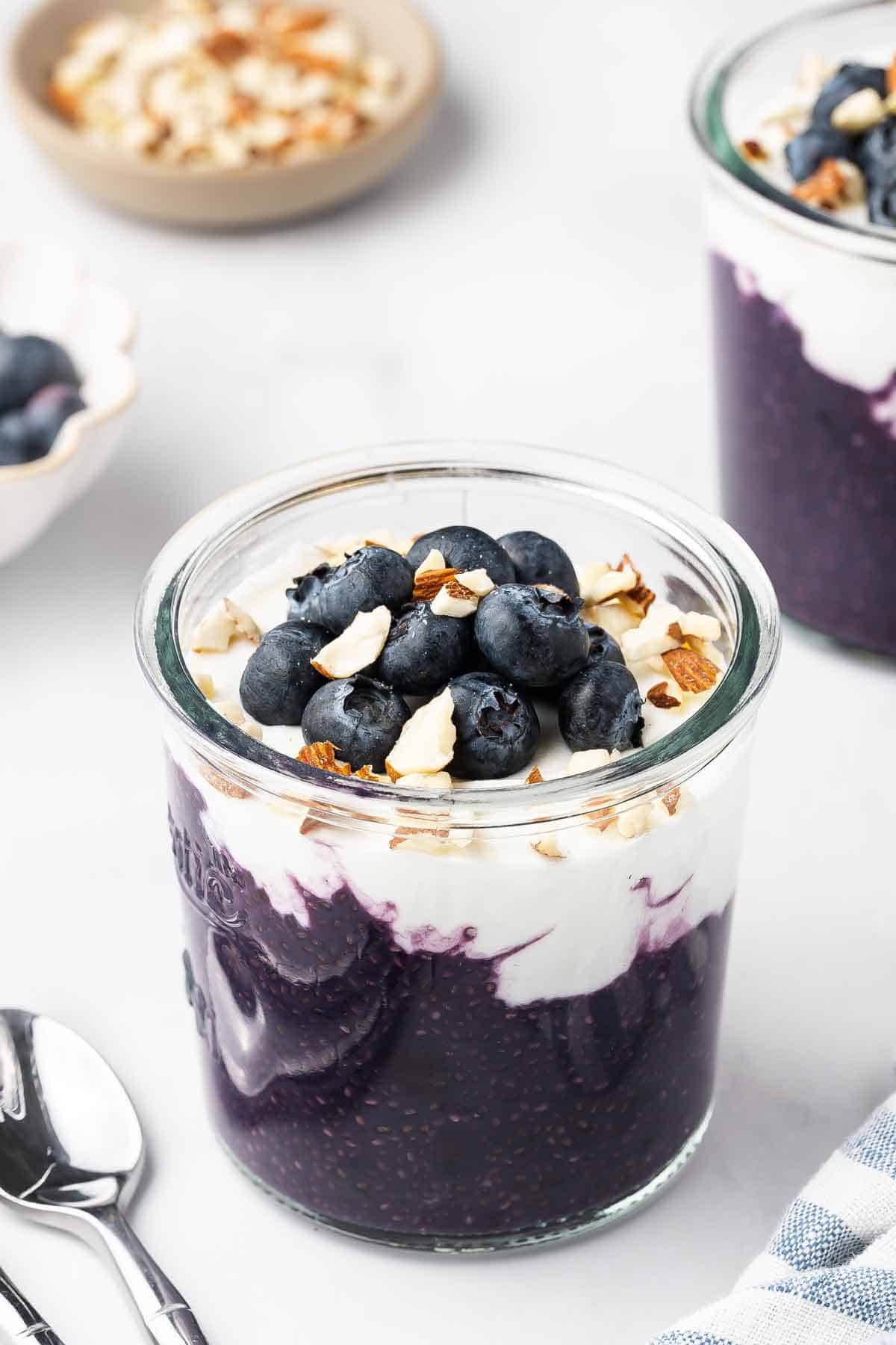 A jar of blueberry chia pudding topped with fresh blueberries, chopped almonds, and yogurt.