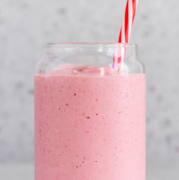 Close up of a glass of pink frozen fruit smoothie with a straw.