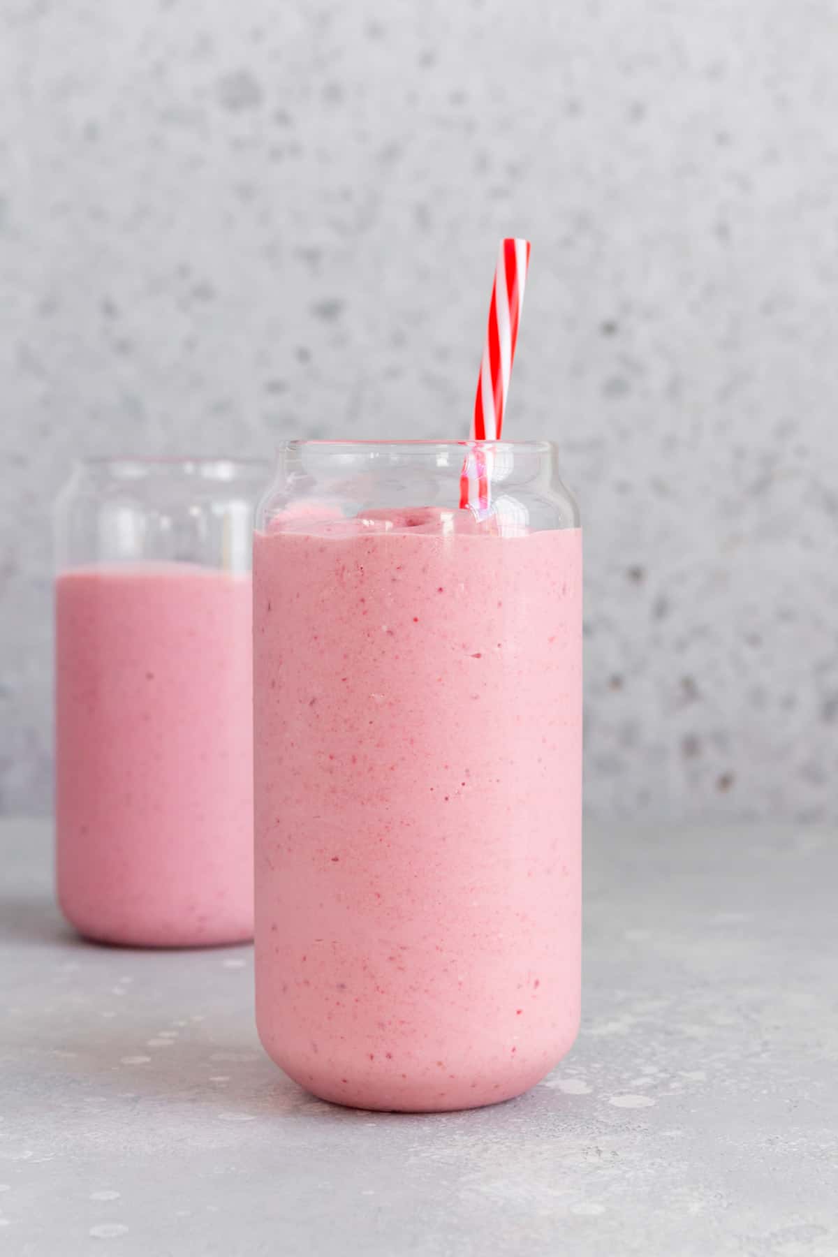 Two glasses of pink frozen fruit smoothie with one in the front and center.