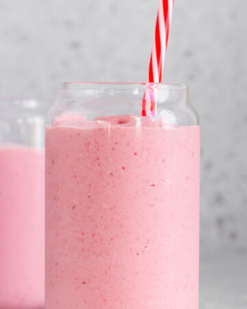 Profile view of a glass of frozen fruit smoothie with a straw with another glass in the background.