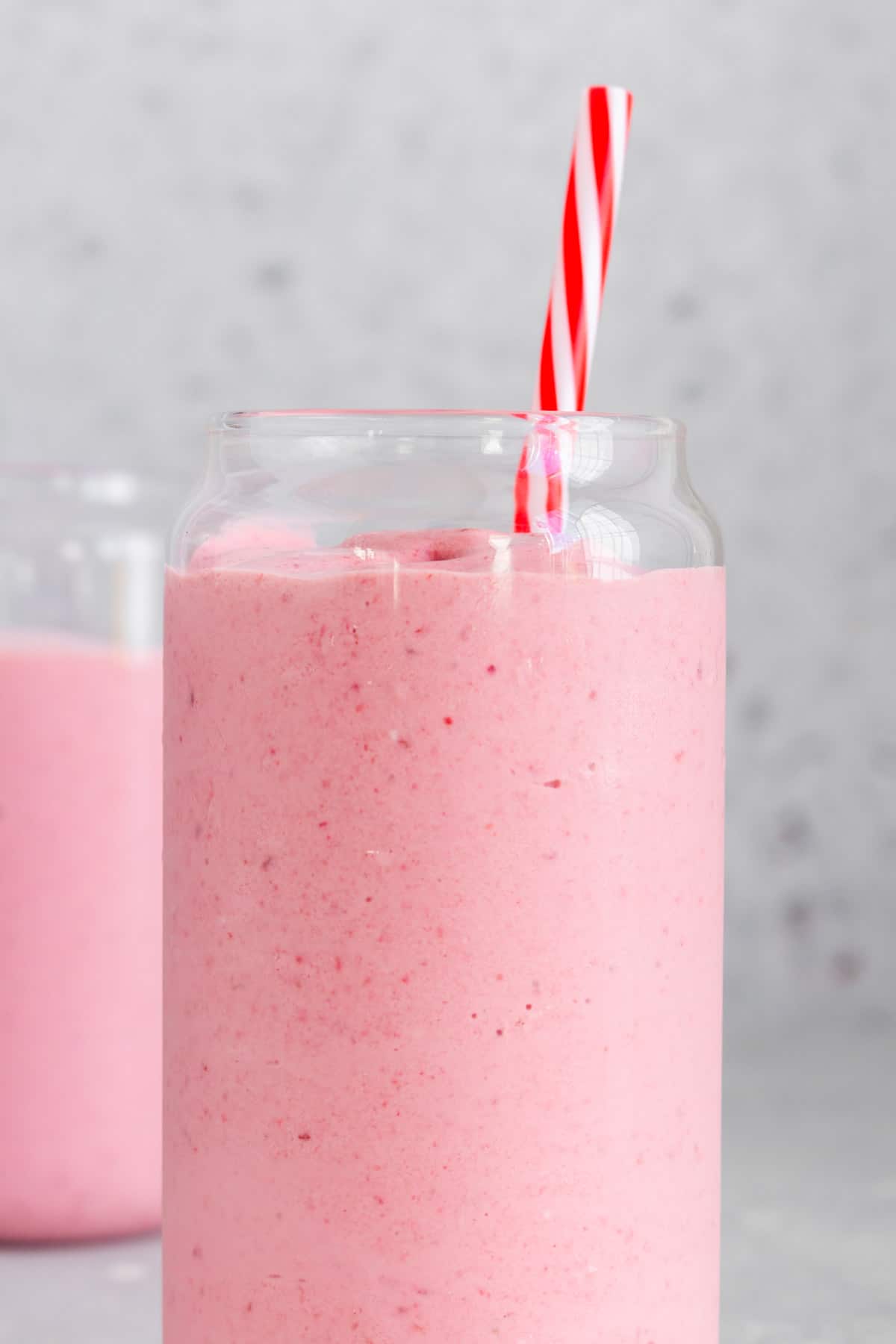 Profile view of a glass of frozen fruit smoothie with a straw with another glass in the background.