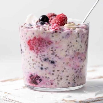 A jar of overnight oats with frozen fruit with a spoon inside.