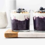 A glass of blueberry chia pudding topped with yogurt and blueberries.
