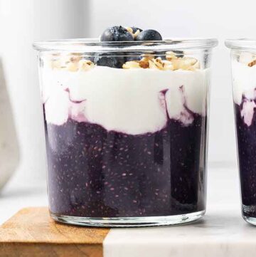 Two glasses of blueberry chia pudding with yogurt and fresh blueberries on top.