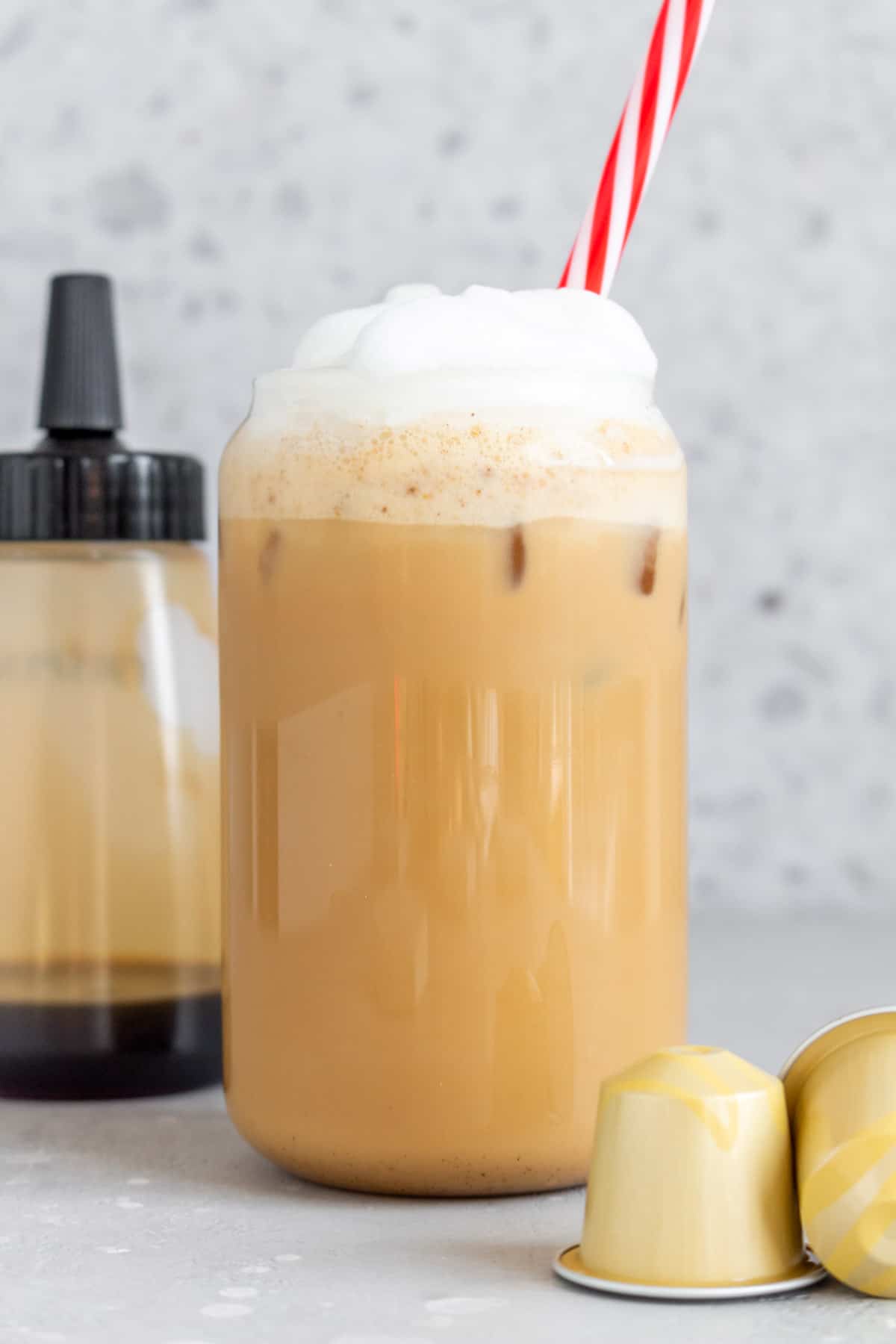 Close view of a glass of brown sugar latte with a striped straw with syrup in the background.