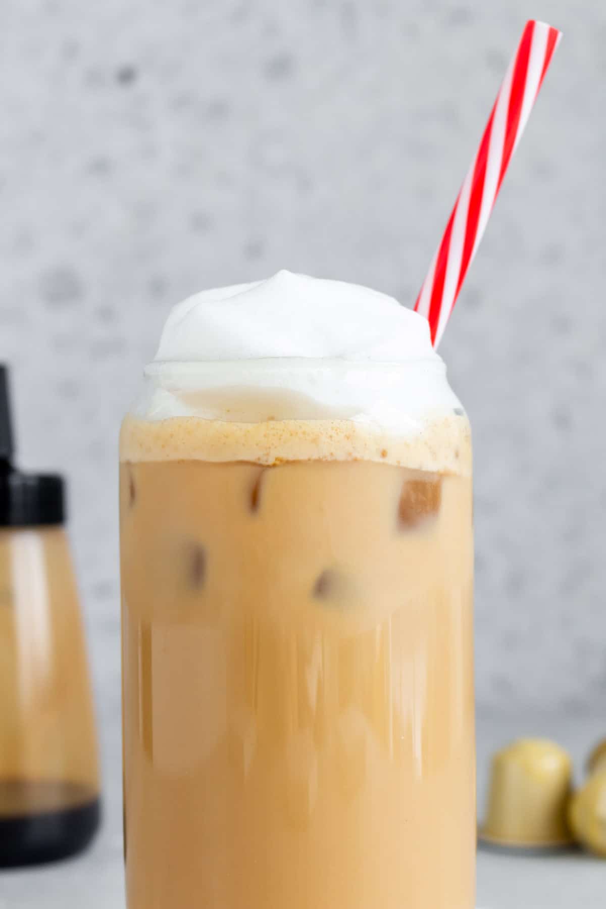 Close up view of a glass of brown sugar latte topped with foam with a striped straw.
