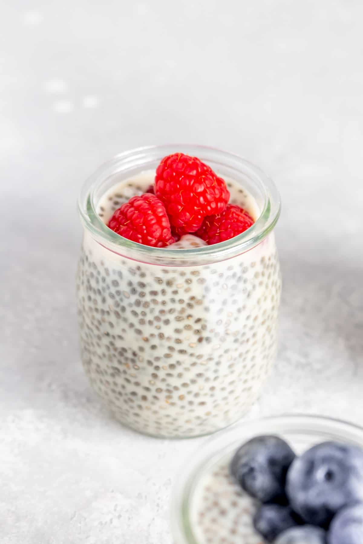 A jar of oat milk chia pudding with raspberries on top.