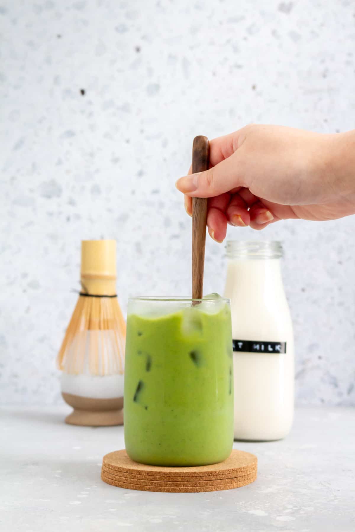 A glass of oat milk matcha latte stirred with a wooden spoon.