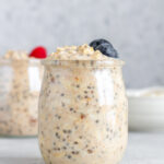 A jar of almond milk overnight oats topped with two blueberries.