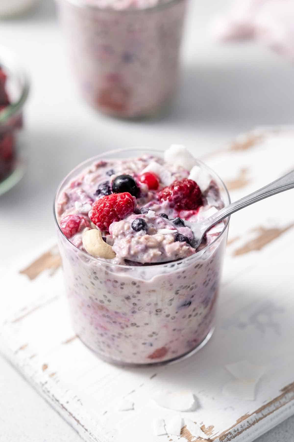 A glass of overnight oats with frozen fruit with a spoonful lifted out.