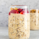 Profile view of a glass of overnight oats with protein powder with some red berries on top.