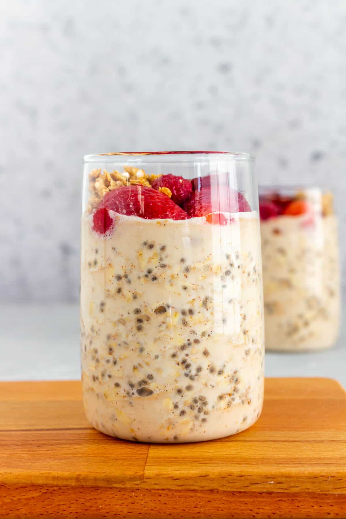 A glass of overnight oats with protein powder topped with berries and granola.