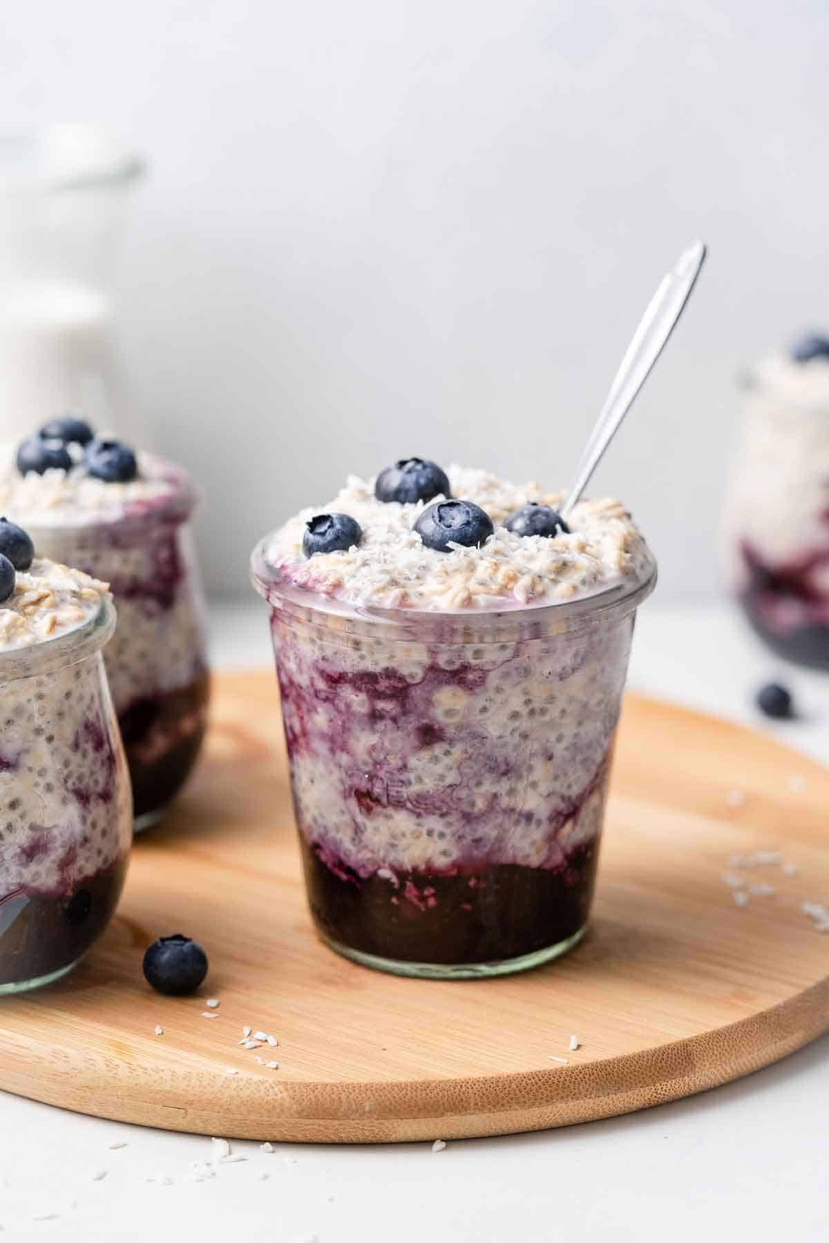 A jar of overnight oats with water with a layer of cooked blueberries mixed into the bottom and fresh blueberries on top.