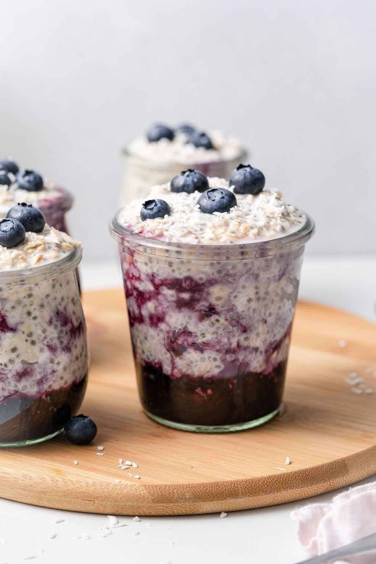 A jar of overnight oats with water with a layer of cooked blueberries and topped with fresh blueberries and coconut.
