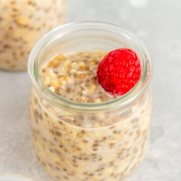 A slightly angled view of a cup of applesauce overnight oats with a raspberry on top.