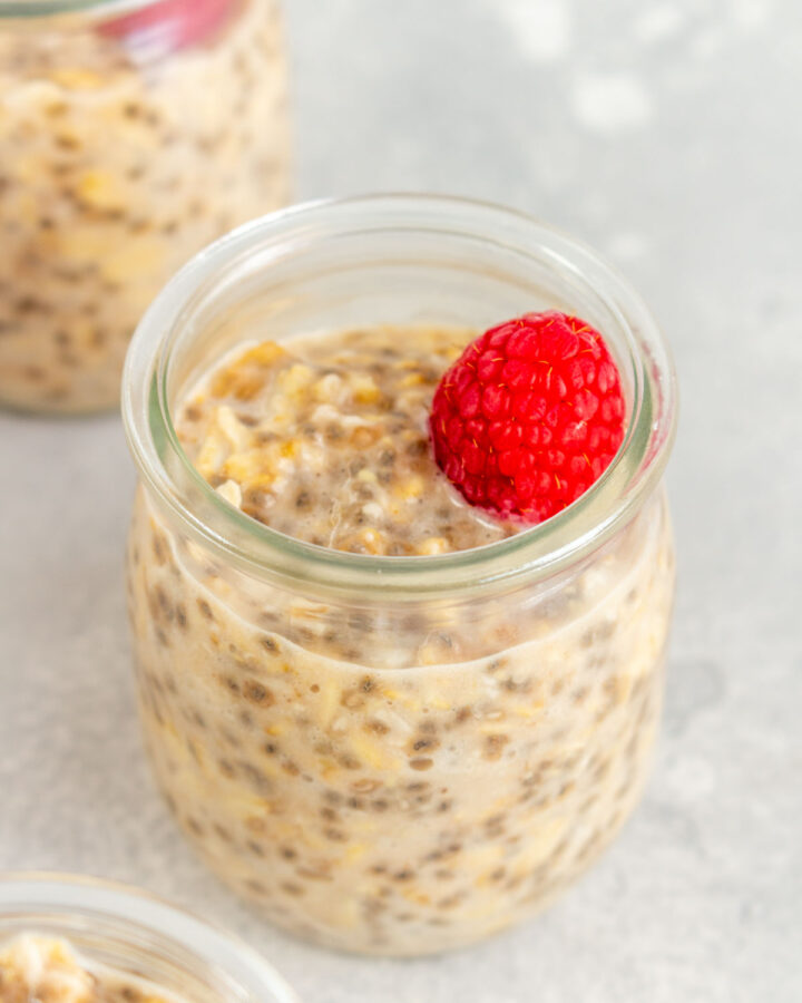 A slightly angled view of a cup of applesauce overnight oats with a raspberry on top.