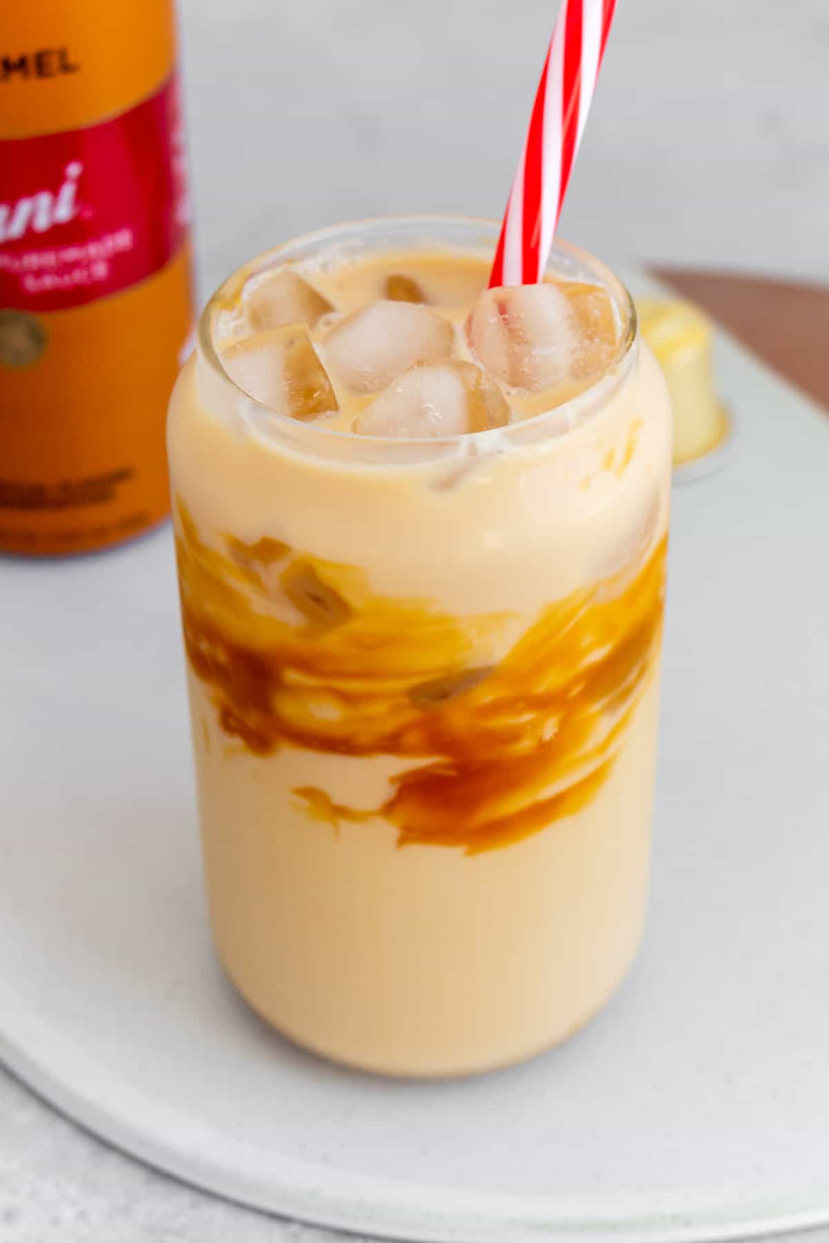 An angled view of a glass of caramel macchiato with a striped straw.