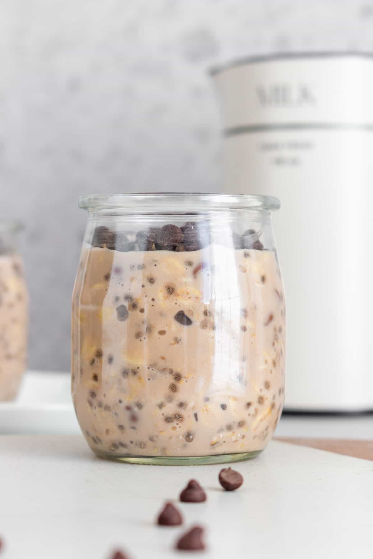 A small cup of chocolate protein overnight oats with mini chocolate chips on top and scattered around.