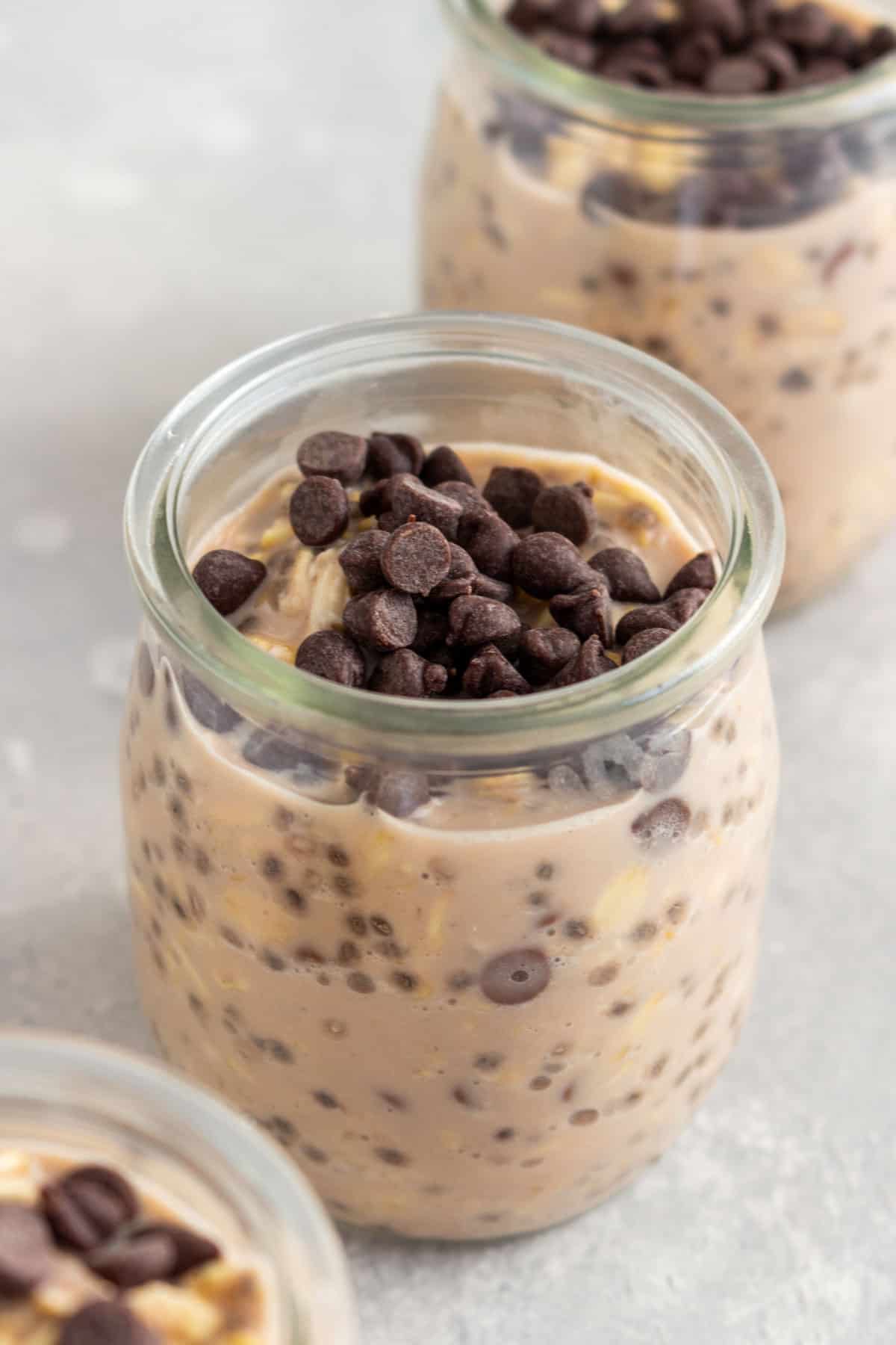 An angled photo of three cups of chocolate protein overnight oats topped with mini chocolate chips.