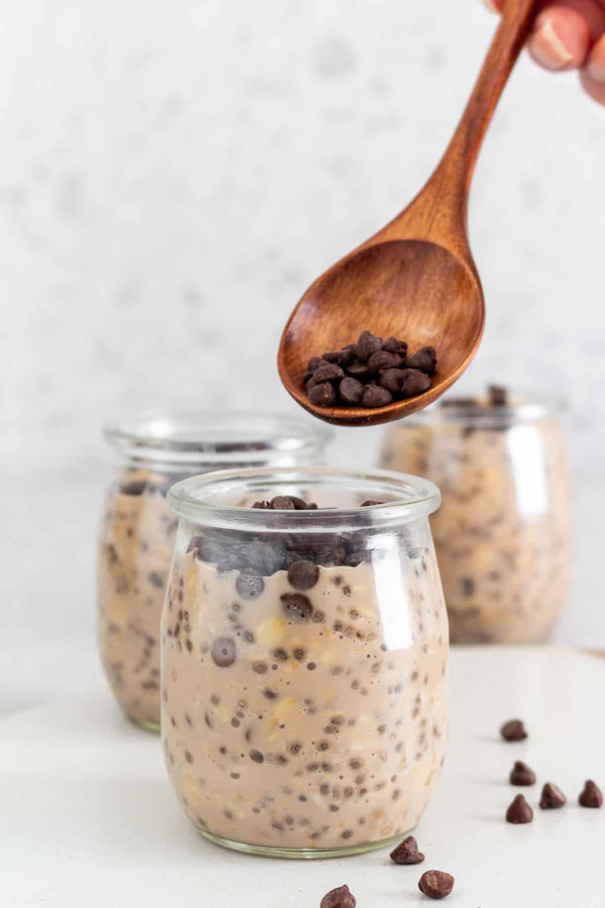 A spoonful of mini chocolate chips spooned over a container of chocolate protein overnight oats.