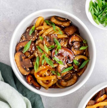 A bowl of mushroom udon topped with green onions and sesame seeds.