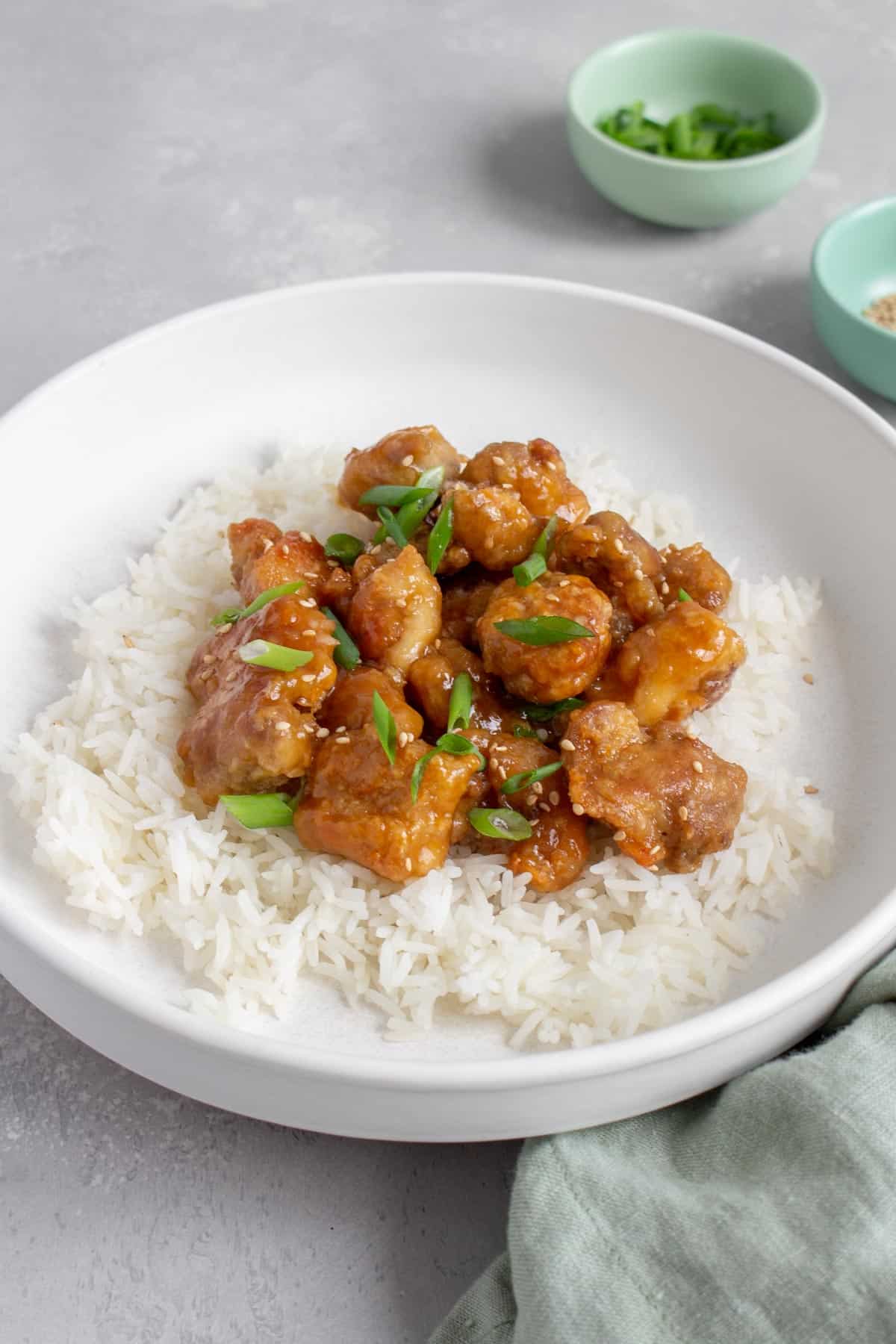 A white plate with rice with orange chicken on top.