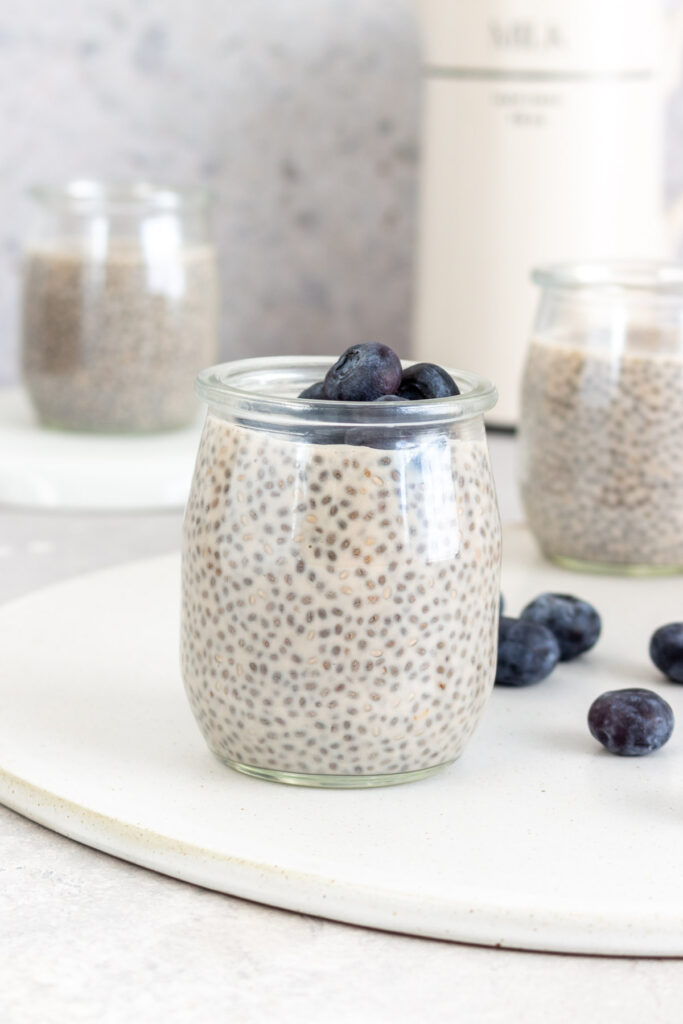 A cup of protein chia pudding topped with fresh blueberries with more scattered around.
