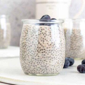 A cup of protein chia pudding with blueberries on top and scattered beside it.