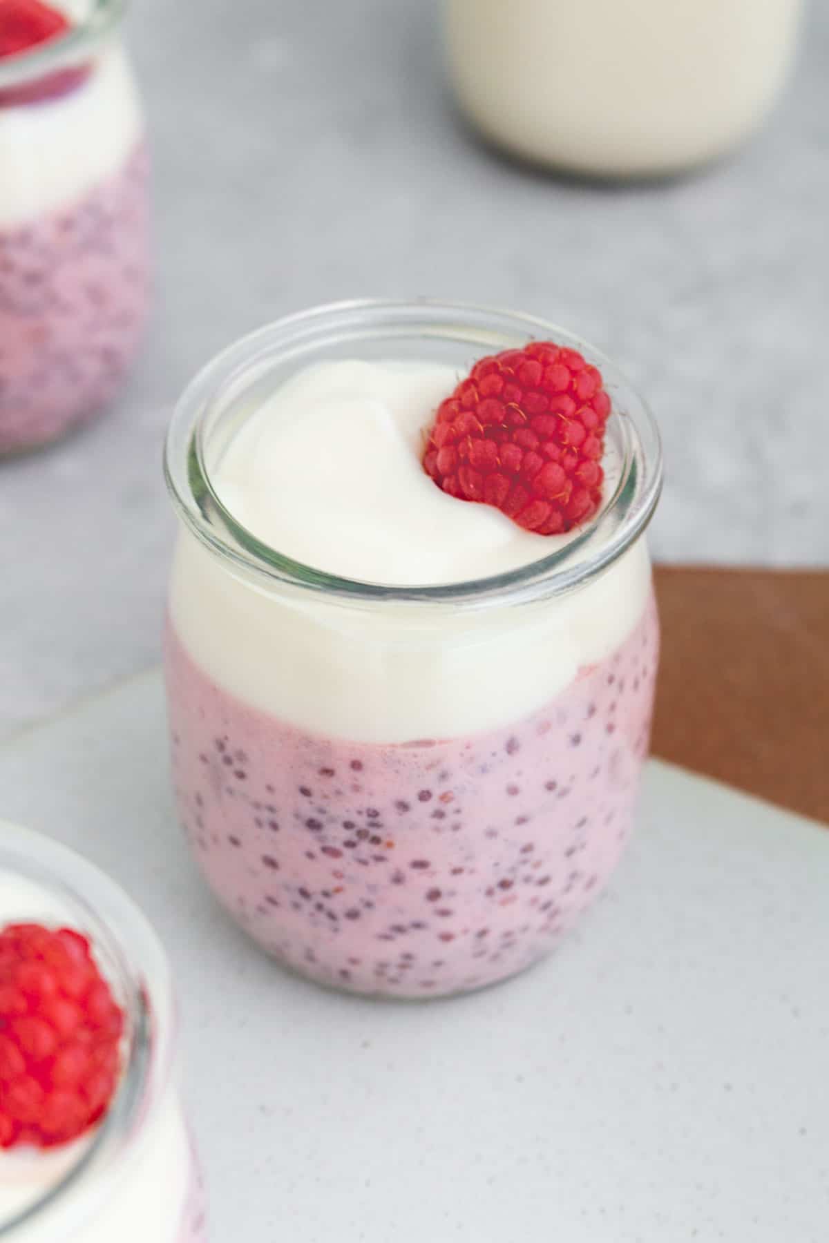 A cup of raspberry chia pudding topped with a layer of yogurt and a raspberry.