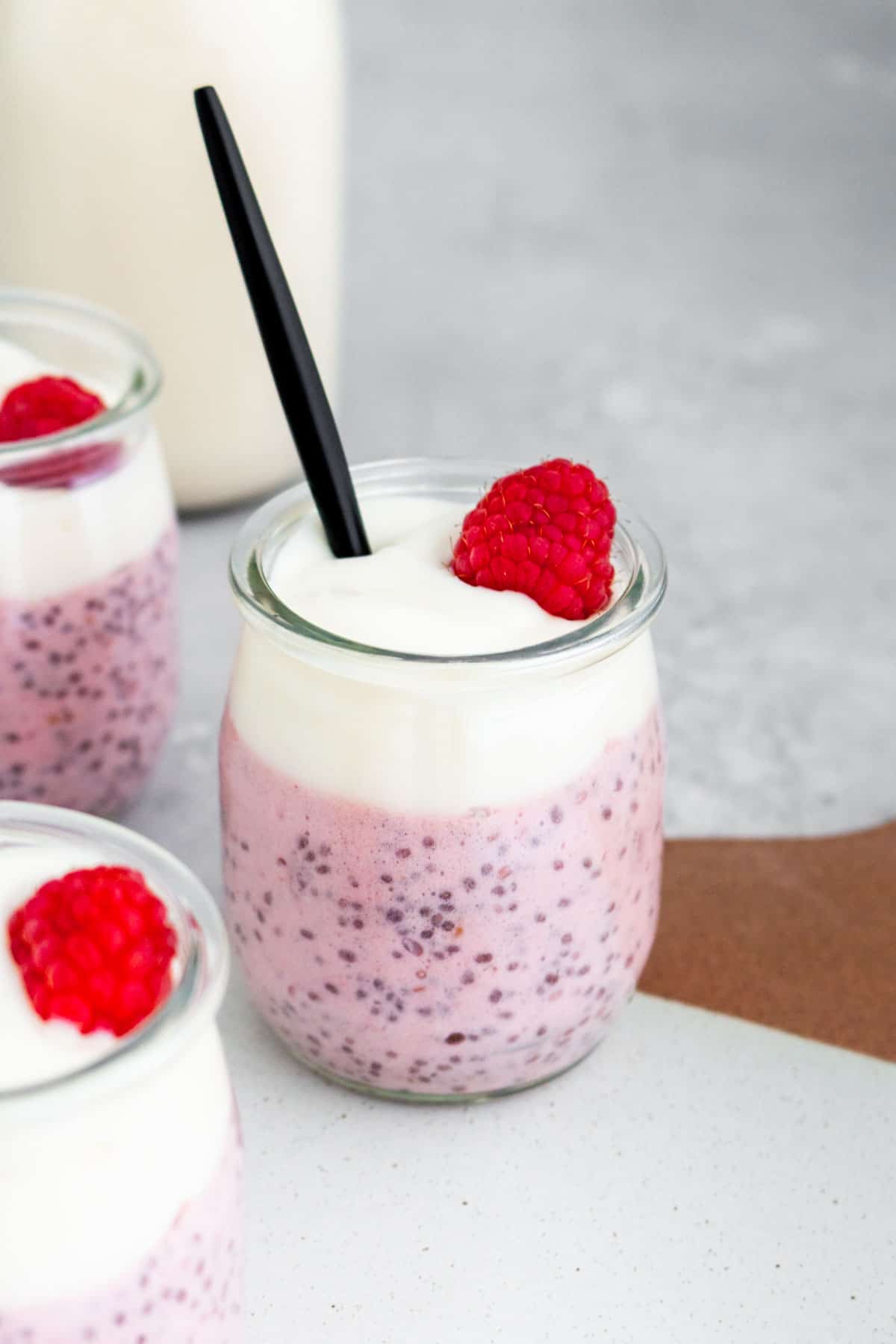 A cup of raspberry chia pudding with yogurt and a fresh raspberry on top with a spoon inside.