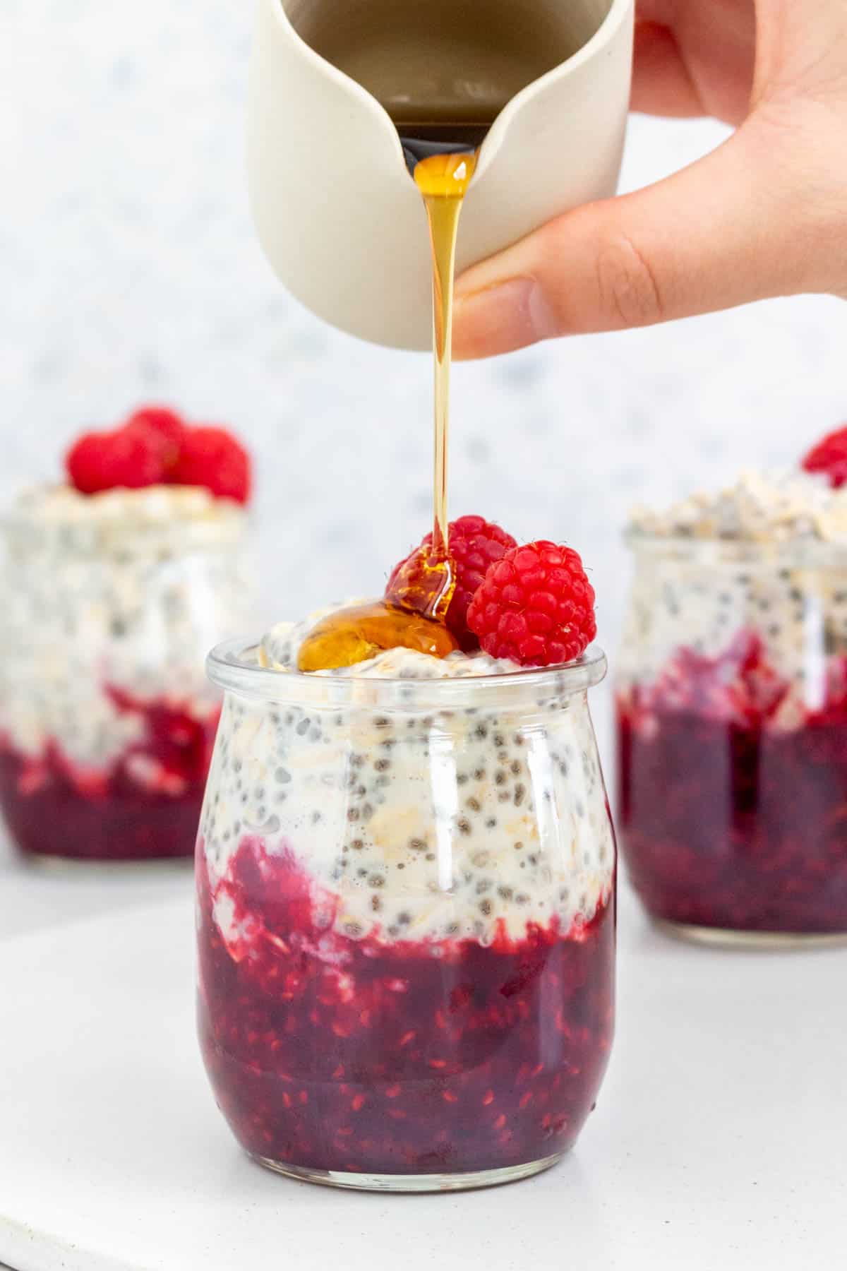 A jar of raspberry overnight oats with maple syrup poured on top.
